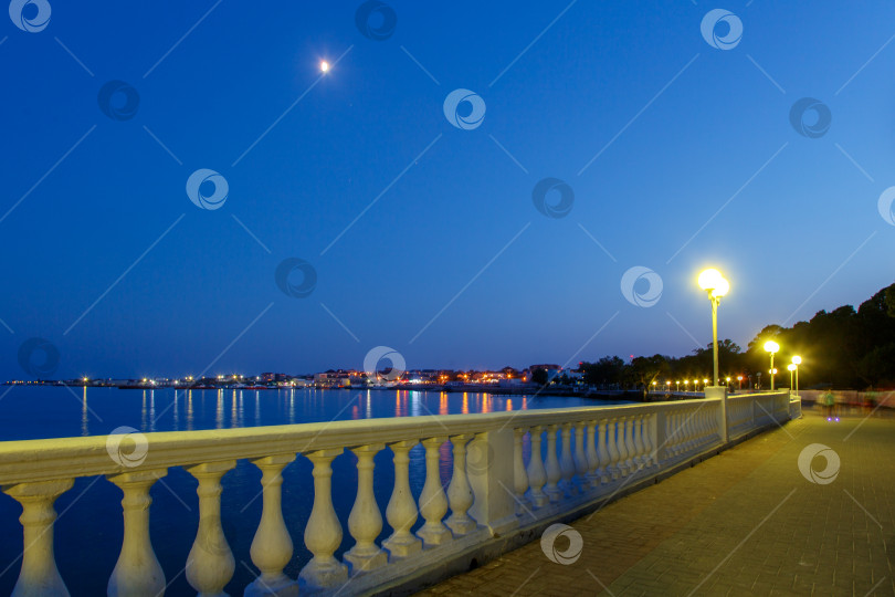 Скачать Курорт Геленджик в вечерних сумерках. Белая балюстрада, набережная. Огни города отражаются в воде Геленджикской бухты. фотосток Ozero