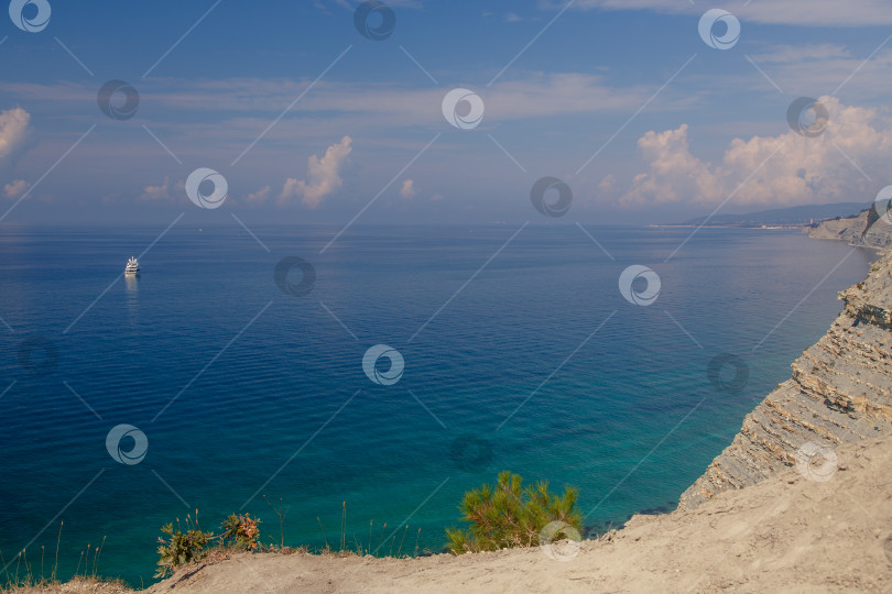 Скачать Большая белая моторная яхта стоит у крутого высокого скалистого берега. На вершине скалы растут сосны. Геленджик, Черное море. Спокойное, гладкое море фотосток Ozero