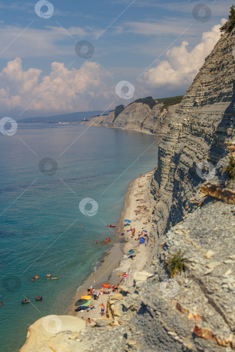 Скачать Курорт Геленджик, пляж Сосновка. Черное море. Высокая белая скала, на вершине которой растут сосны. Пляж у подножия скалы. Маяк на заднем плане фотосток Ozero