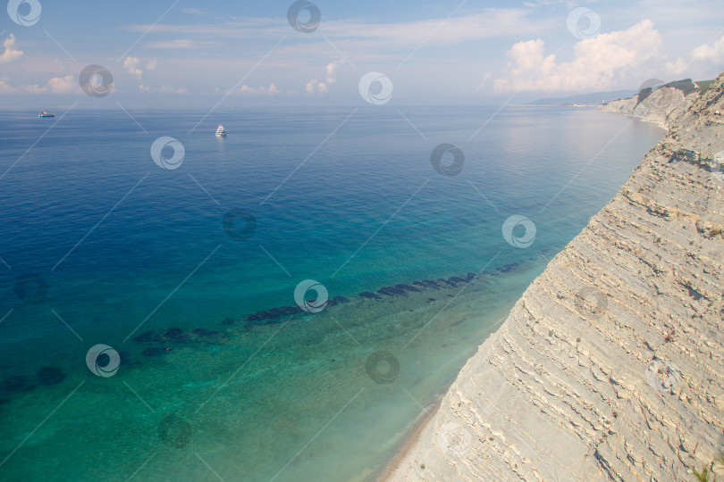 Скачать Большая белая моторная яхта стоит у крутого высокого скалистого берега. На вершине скалы растут сосны. Геленджик, Черное море. Спокойное, гладкое море фотосток Ozero