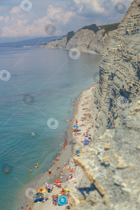 Скачать Пляж Сосновка, Геленджик. Люди загорают и купаются на пляже у подножия высокой белой скалы. Прозрачная вода, солнце фотосток Ozero