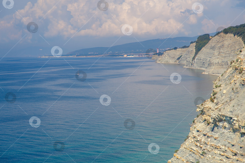 Скачать Курорт Геленджик, пляж Сосновка. Черное море. Высокая белая скала, на вершине которой растут сосны. Пляж у подножия скалы. Маяк на заднем плане фотосток Ozero