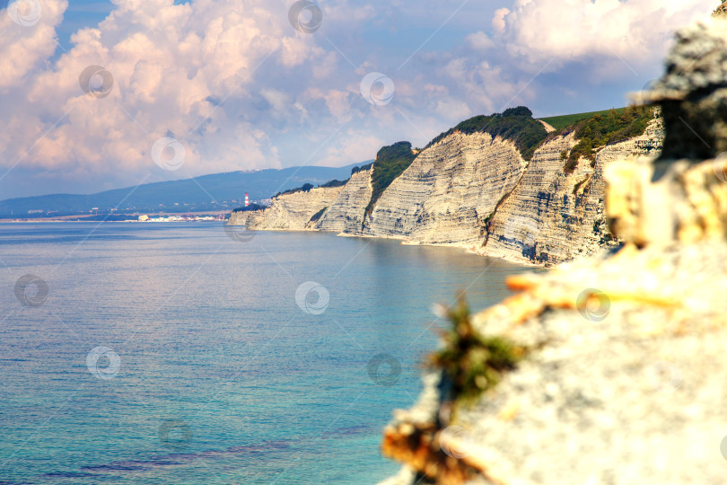 Скачать Курорт Геленджик, пляж Сосновка. Черное море. Высокая белая скала, на вершине которой растут сосны. Пляж у подножия скалы. Маяк на заднем плане фотосток Ozero