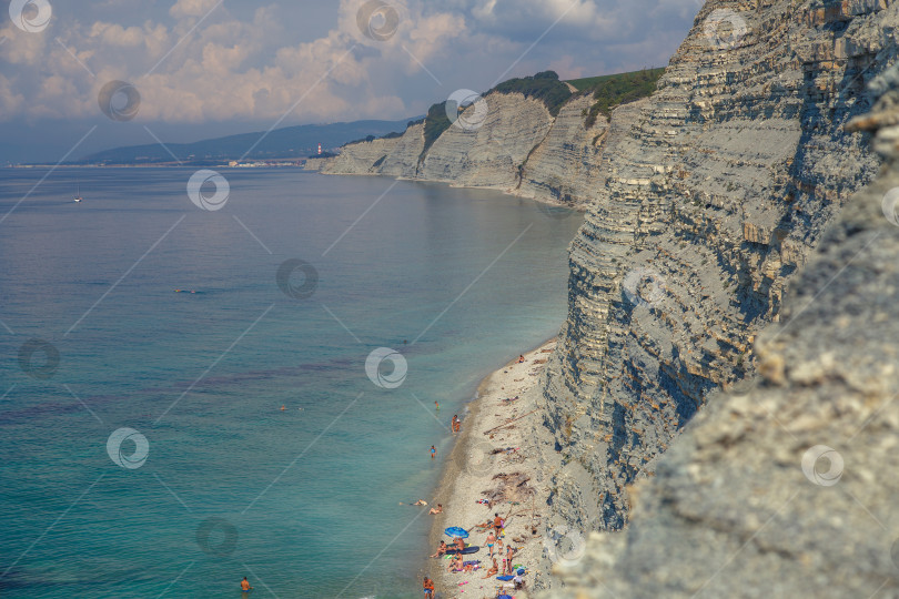 Скачать Курорт Геленджик, пляж Сосновка. Черное море. Высокая белая скала, на вершине которой растут сосны. Пляж у подножия скалы. Маяк на заднем плане фотосток Ozero