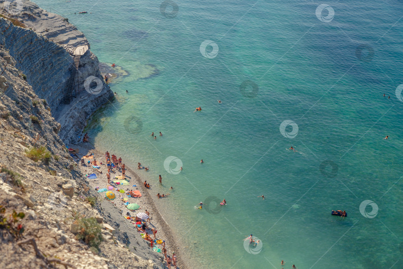 Скачать Геленджик. Пляж Сосновка. Высокая белая скала и пляж у подножия обрыва. Чистое теплое море. Люди будут загорать на пляже. фотосток Ozero