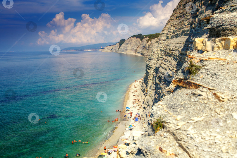 Скачать Курорт Геленджик, пляж Сосновка. Черное море. Высокая белая скала, на вершине которой растут сосны. Пляж у подножия скалы. Маяк на заднем плане фотосток Ozero