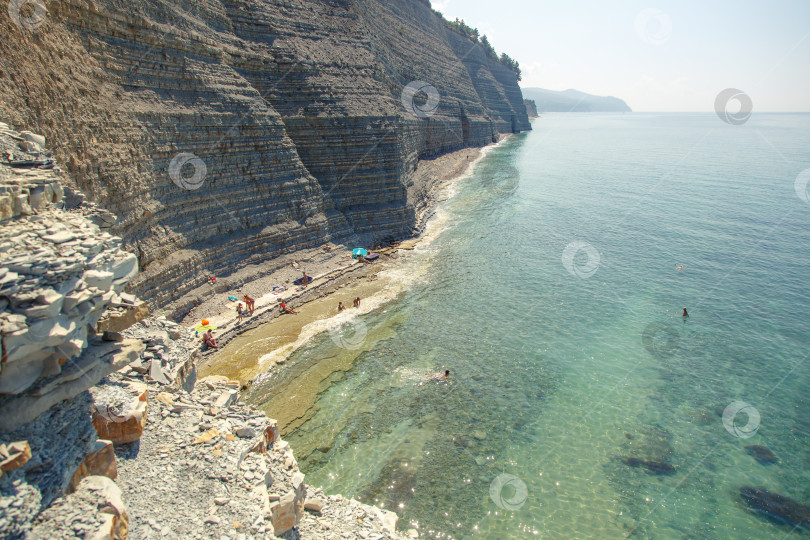 Скачать Курот Геленджик. Пляж Сосновка. Высокая белая скала и пляж у подножия обрыва. Чистое теплое море. Люди будут загорать на пляже. фотосток Ozero