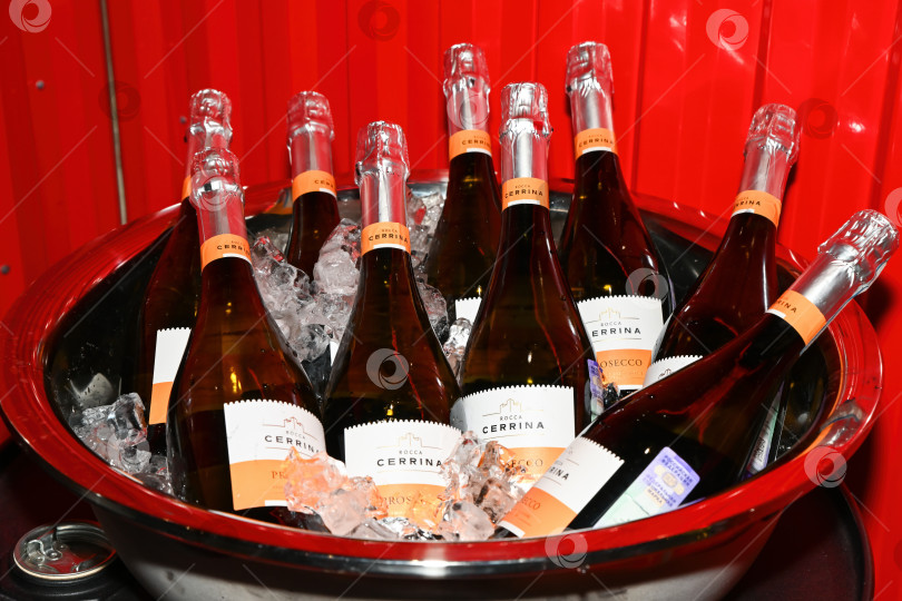 Скачать Владивосток, Россия, 20 августа 2025 года - Бутылки вина Rocca Cerrina Prosecco со льдом в большом металлическом ведерке на красном фоне на праздничном мероприятии. фотосток Ozero