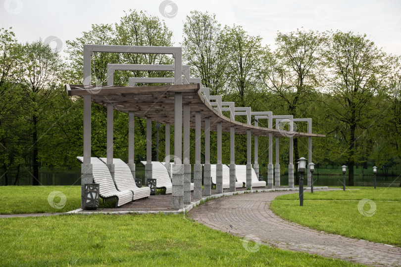 Скачать Современная парковая беседка с изогнутыми скамейками и пышной зеленью весной фотосток Ozero