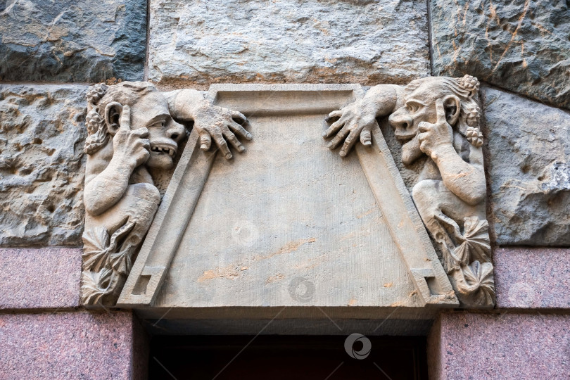 Скачать Каменные горгульи выглядывают из-за архитектурной рамы на стене исторического здания фотосток Ozero