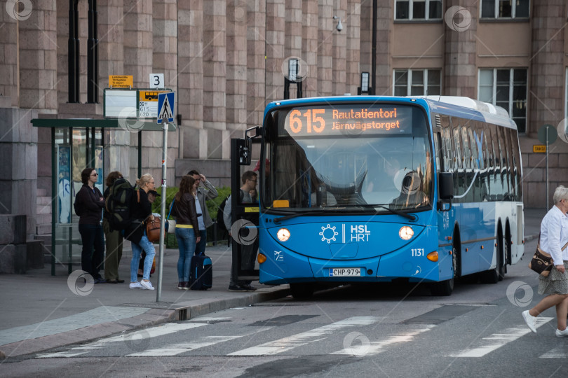 Скачать Синий городской автобус с разнообразными пассажирами садится на городской остановке фотосток Ozero
