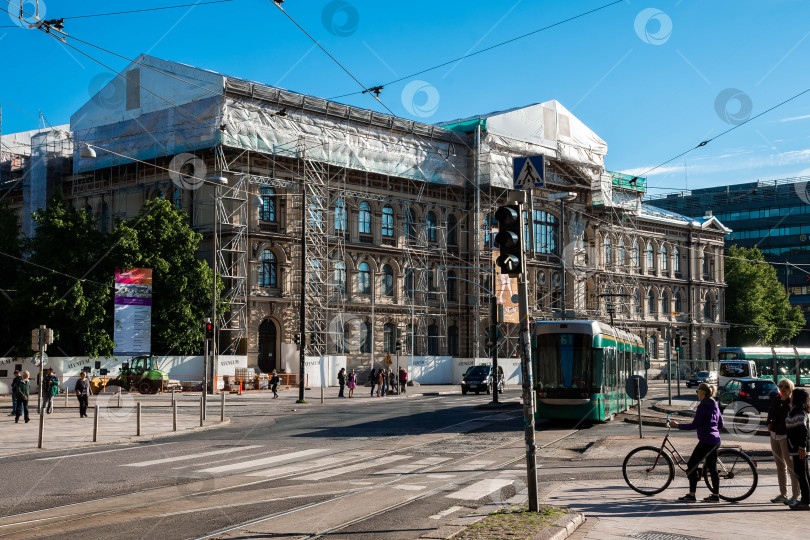 Скачать Историческое здание в стадии реконструкции с трамваем и пешеходами на оживленной городской улице фотосток Ozero