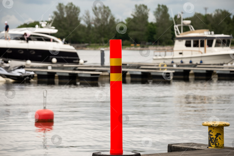 Скачать Ярко-красный кнехт у пристани для яхт с пришвартованными лодками на тихой набережной фотосток Ozero