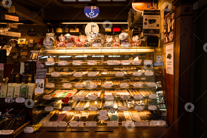 Скачать Витрина пекарни с разнообразной выпечкой и шоколадом в уютном интерьере магазина фотосток Ozero