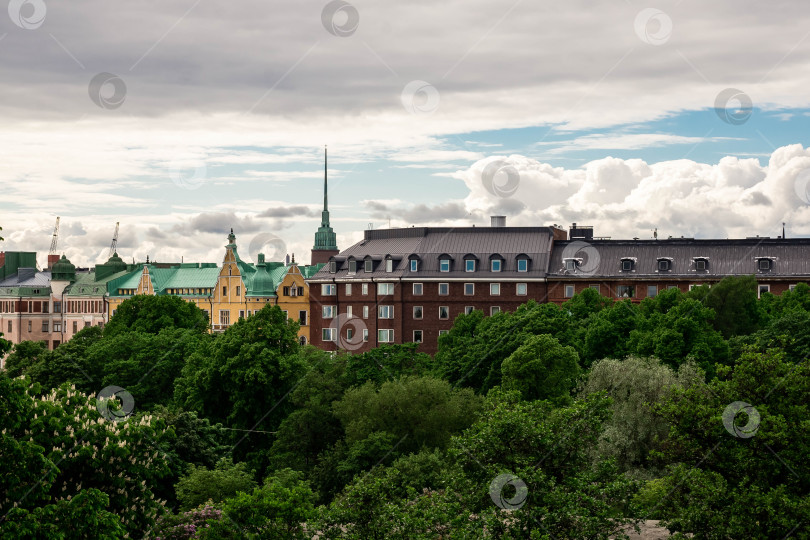 Скачать Живописный вид на городской пейзаж с историческими зданиями и пышной зеленью под пасмурным небом фотосток Ozero