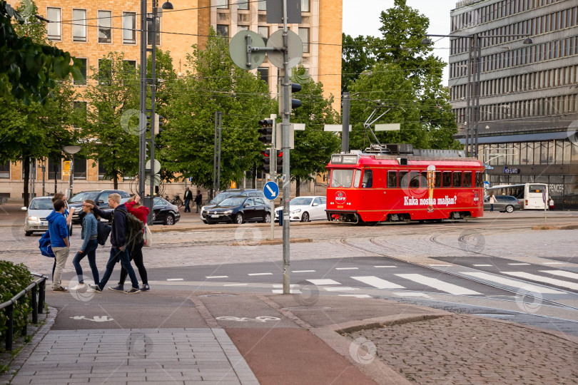Скачать Красный трамвай проезжает через городской перекресток с людьми, переходящими улицу фотосток Ozero