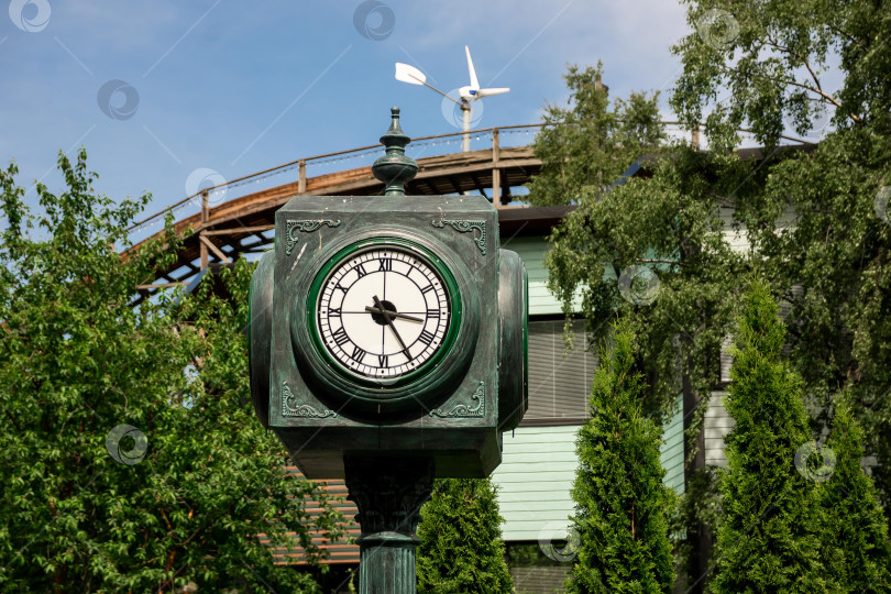 Скачать Старинные уличные часы с ветряной турбиной и американскими горками на заднем плане фотосток Ozero