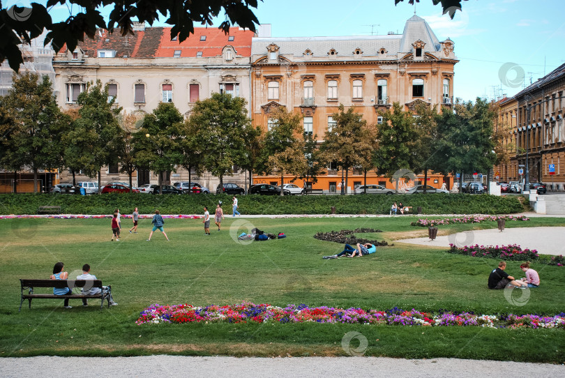 Скачать Люди отдыхают в европейском городском парке с историческими зданиями фотосток Ozero