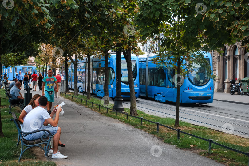 Скачать Голубой трамвайчик в городском парке, рядом с которым отдыхают молодые люди кавказской национальности фотосток Ozero