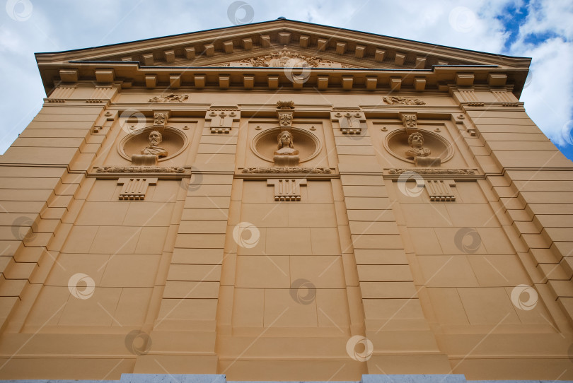 Скачать Фасад здания в неоклассическом стиле со скульптурными рельефами и пилястрами на фоне облачного неба фотосток Ozero