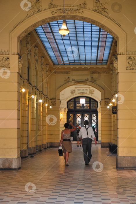 Скачать Интерьер исторической европейской галереи с людьми, прогуливающимися под сводчатым потолком фотосток Ozero