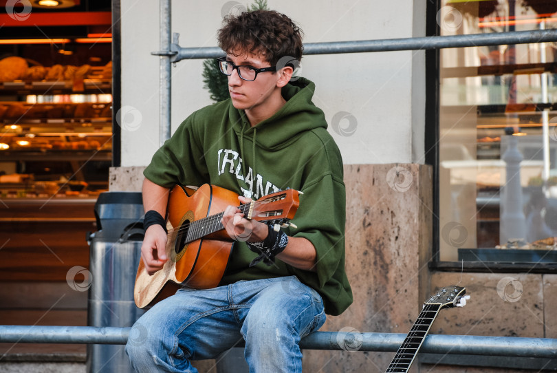 Скачать Молодой кавказец играет на акустической гитаре на уличной скамейке фотосток Ozero