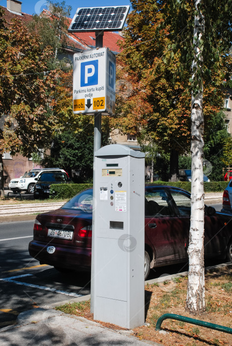Скачать Парковочный счетчик на солнечных батареях на городской улице с автомобилями и деревьями фотосток Ozero