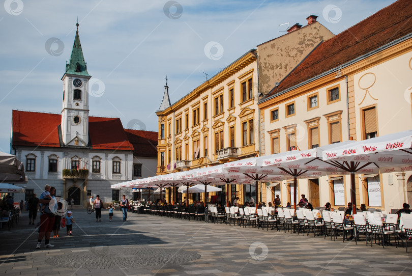 Скачать Историческая европейская площадь с людьми, обедающими на улице, и средневековой архитектурой на заднем плане фотосток Ozero