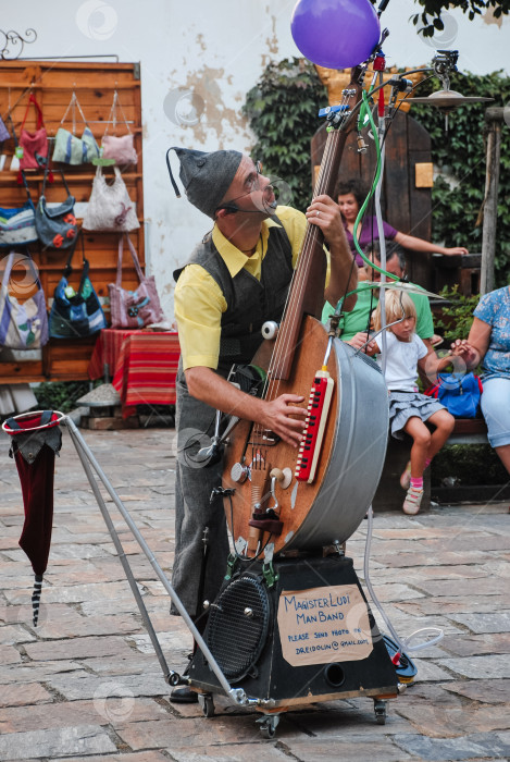 Скачать Уличный исполнитель, играющий на уникальном инструменте, кавказский мужчина для взрослых развлекает публику на открытом воздухе фотосток Ozero
