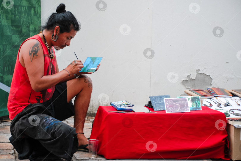 Скачать Испаноязычный художник-мужчина рисует на улице с выставкой произведений искусства фотосток Ozero