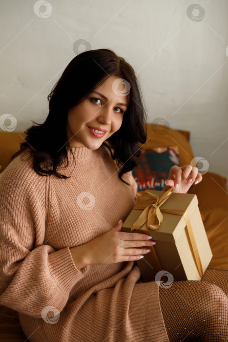 Скачать женщина в свитере сидит на кровати в комнате, держит подарок фотосток Ozero