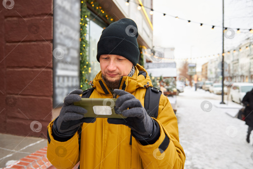 Скачать мужчина в шляпе и куртке держит в руках смартфон фотосток Ozero