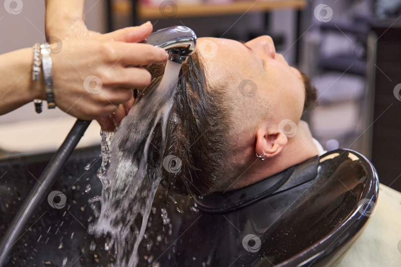 Скачать парикмахер моет волосы молодому человеку в раковине фотосток Ozero