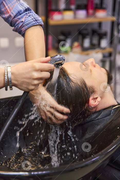 Скачать парикмахер моет волосы молодому человеку в раковине в парикмахерской фотосток Ozero