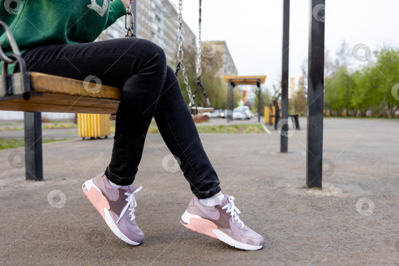 Скачать Женщина в толстовке и джинсах сидит на качелях фотосток Ozero