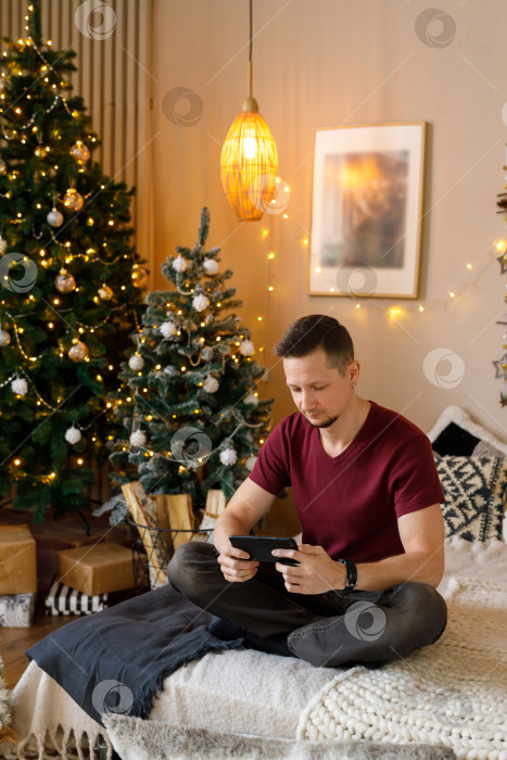 Скачать мужчина сидит на кровати, держа в руках смартфон фотосток Ozero