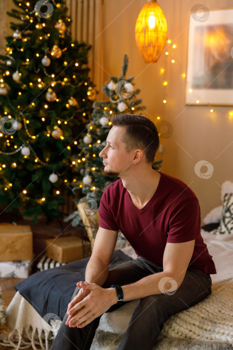 Скачать мужчина сидит на кровати в комнате, украшенной к Рождеству фотосток Ozero