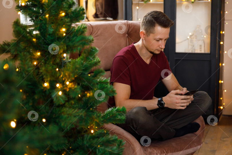 Скачать мужчина сидит в кресле, держа в руках смартфон фотосток Ozero