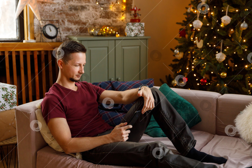 Скачать мужчина сидит на диване, держа в руках смартфон фотосток Ozero