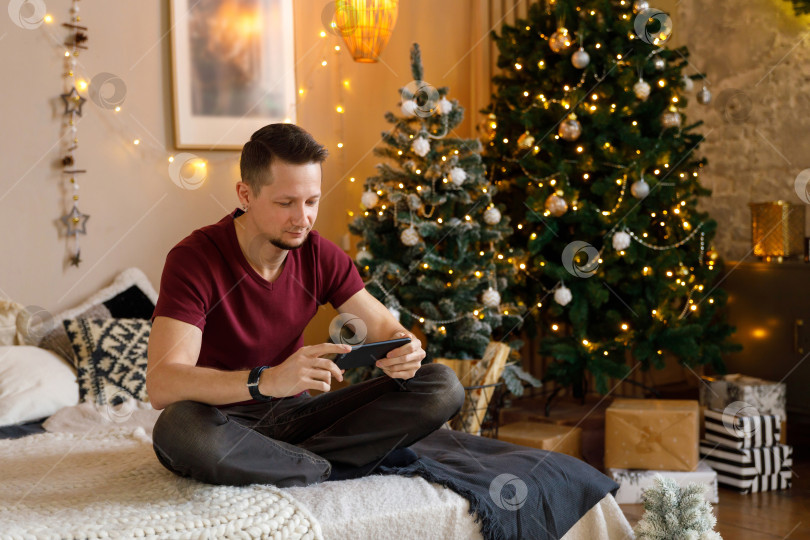 Скачать мужчина сидит на кровати, держа в руках смартфон фотосток Ozero