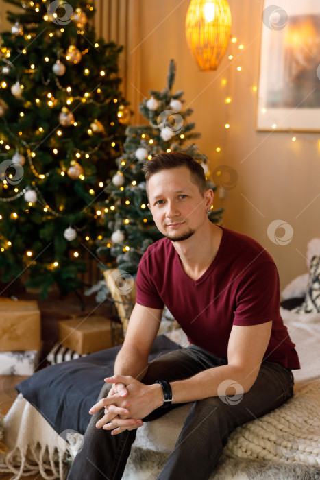 Скачать мужчина сидит на кровати в комнате, украшенной к Рождеству фотосток Ozero