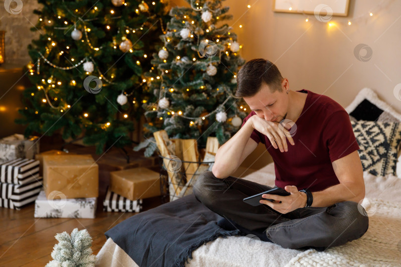 Скачать брюнет сидит на кровати, держа в руках смартфон фотосток Ozero