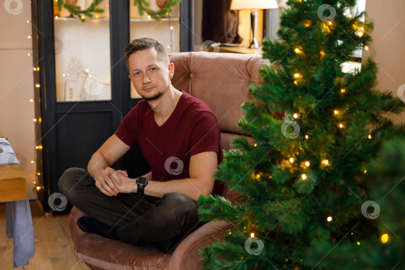 Скачать мужчина сидит в кресле в комнате, украшенной к Рождеству фотосток Ozero