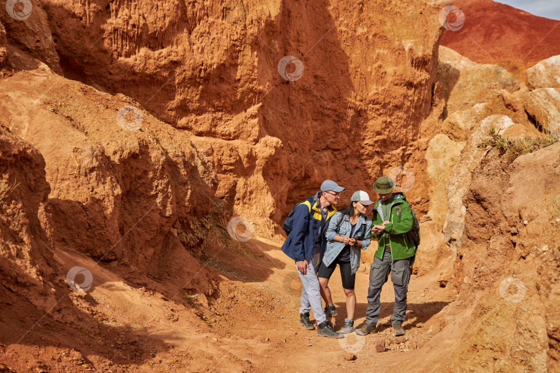 Скачать трое друзей, женщина и мужчина-туристы, стоят в песчаном карьере и смотрят на часы фотосток Ozero