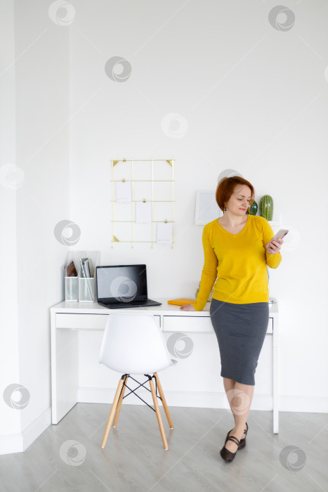 Скачать женщина стоит у белого стола и смотрит в смартфон фотосток Ozero