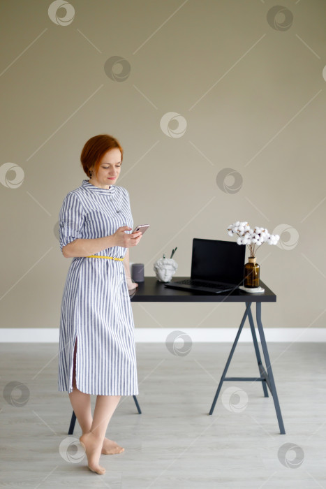 Скачать женщина в платье на фоне бежевой стены со смартфоном в руке фотосток Ozero