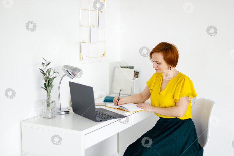 Скачать женщина сидит за белым столом и составляет план на день в блокноте фотосток Ozero