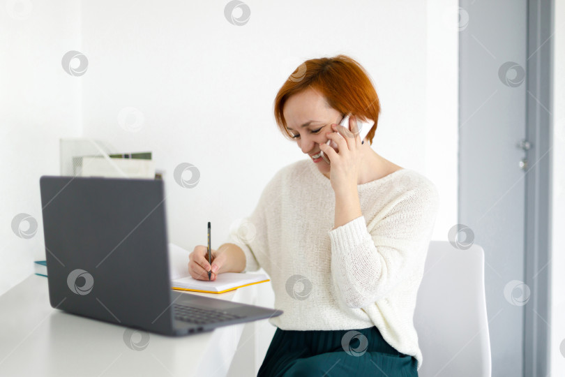 Скачать женщина сидит за белым столом и разговаривает по телефону с клиентом фотосток Ozero