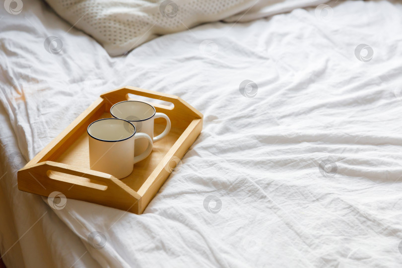 Скачать деревянный поднос и две белые кружки на кровати на белой простыне фотосток Ozero