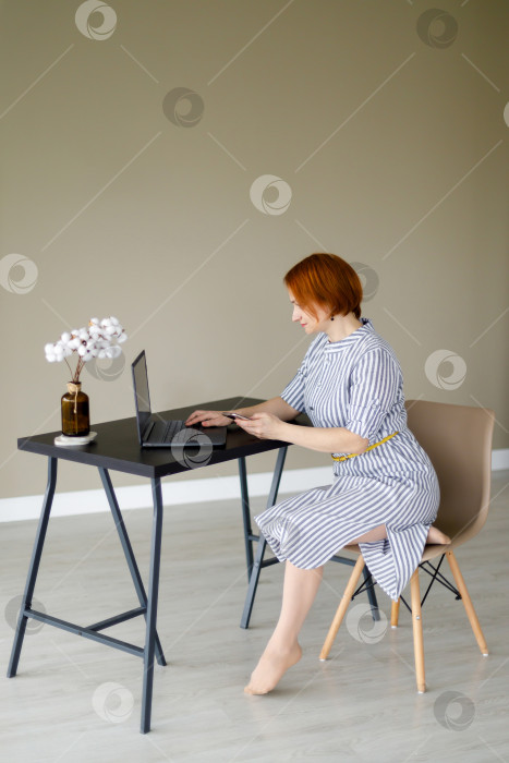 Скачать женщина сидит на фоне бежевой стены, работает за ноутбуком фотосток Ozero